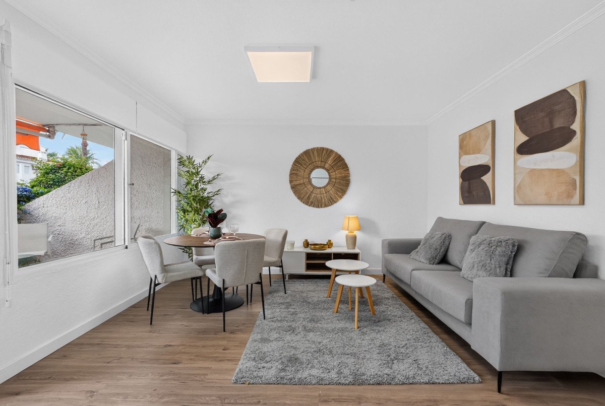 Modern living and dining area with grey sofa, dining table, and large window overlooking greenery.