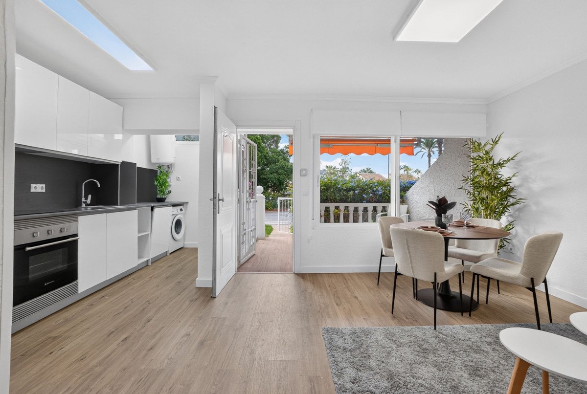 Modern kitchen and dining area with a view of a terrace and lush greenery through the windows.