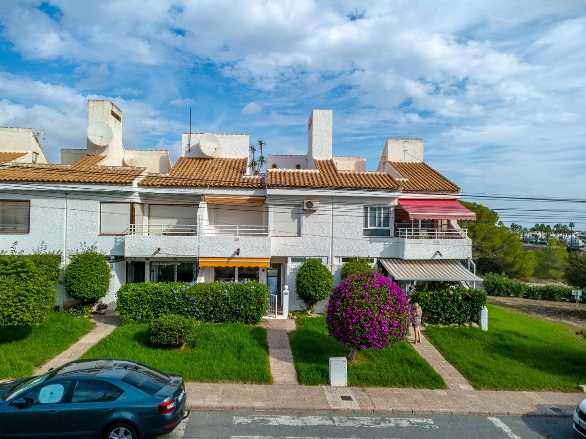 Terraced houses with green lawns, lush bushes, a flowering bougainvillea tree, and a balcony with red awning.