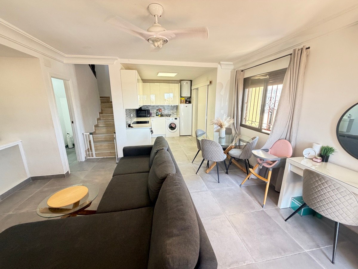Modern open-plan living, dining, and kitchen area with a large sofa, dining table, and kitchen appliances.