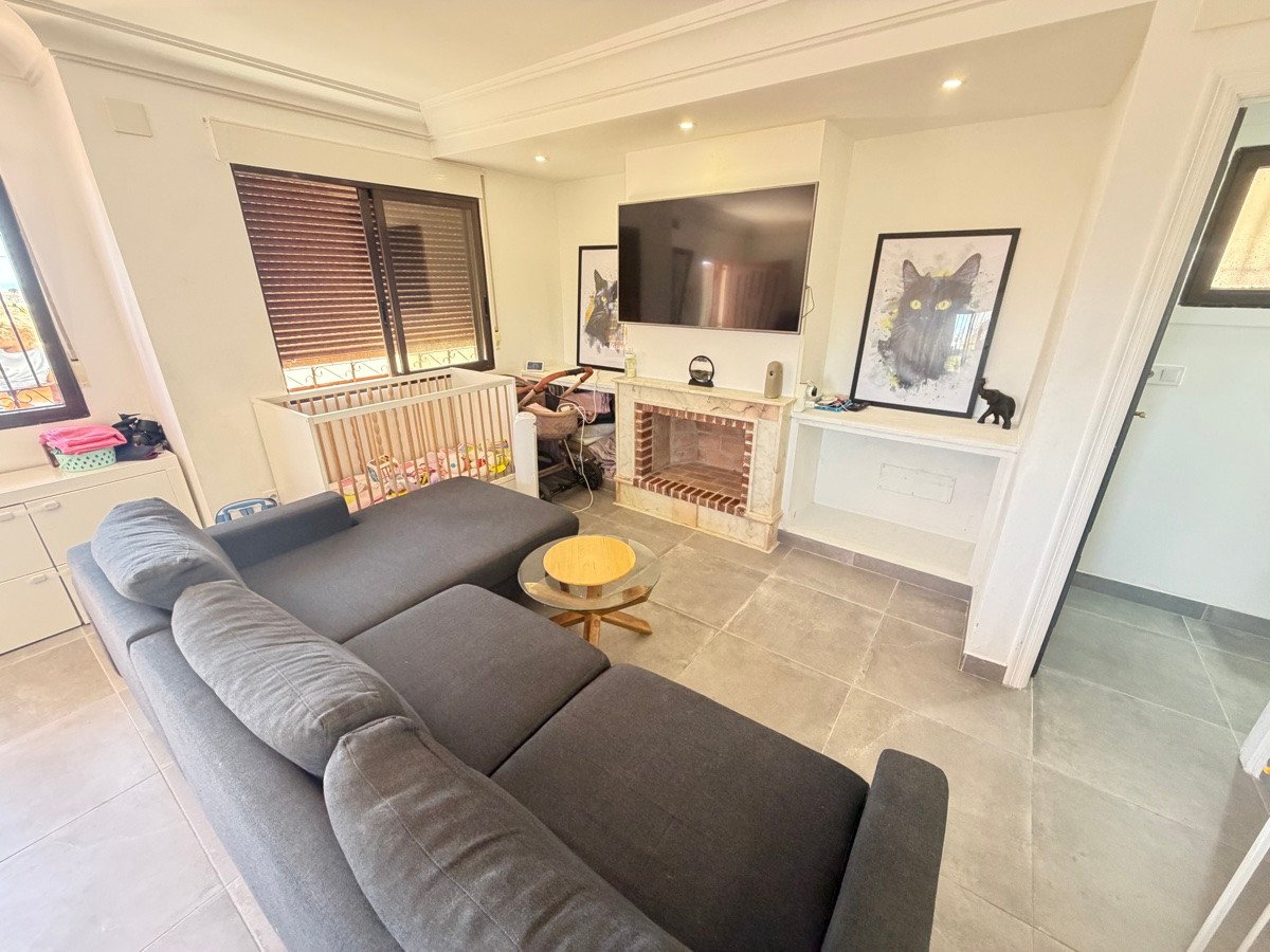 Modern living room with a large sectional sofa, fireplace, TV, and a crib near the window. Features artwork of a black cat.