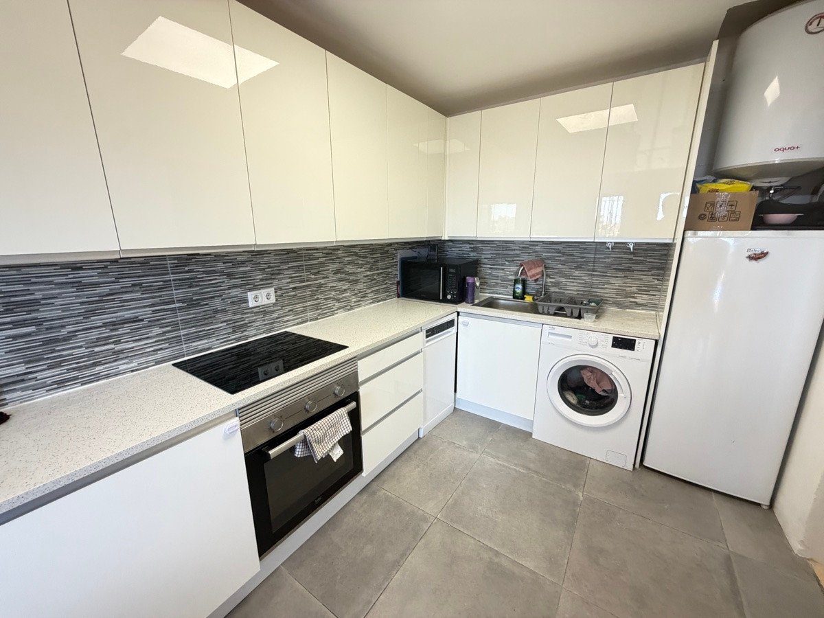 Modern white kitchen with sleek cabinets, induction hob, oven, washing machine, refrigerator, microwave, and sink.