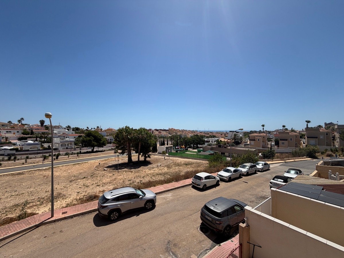 View of a residential street with parked cars and houses under a clear blue sky.