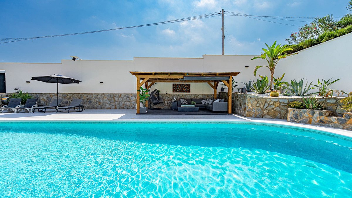 Outdoor pool area with patio seating, lounge chairs, and tropical plants