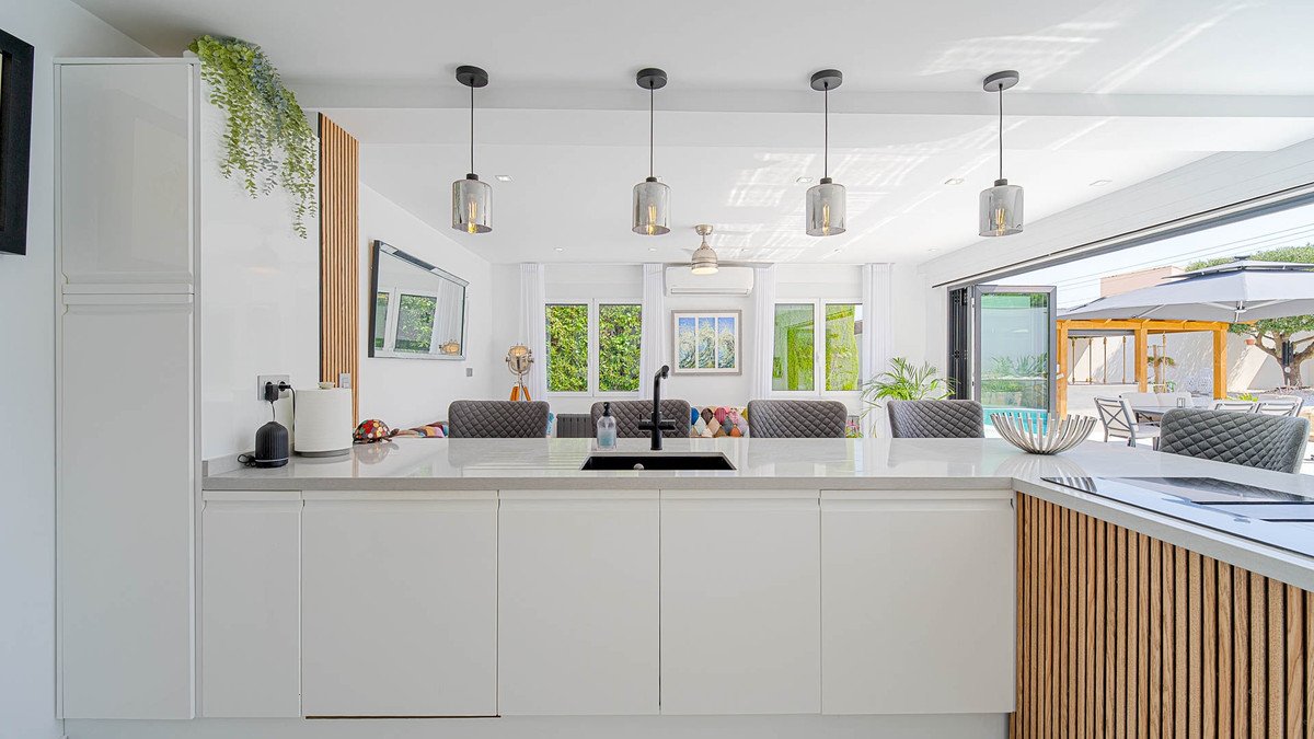 Modern kitchen with white cabinets, pendant lights, and pool view through large windows