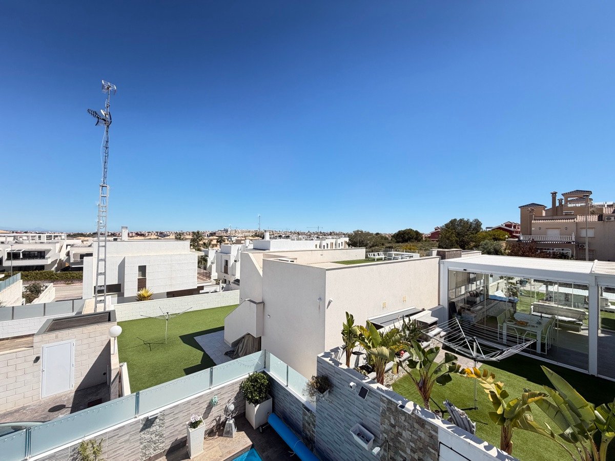 Modern houses with rooftop terraces, artificial grass, and outdoor seating under a clear blue sky.