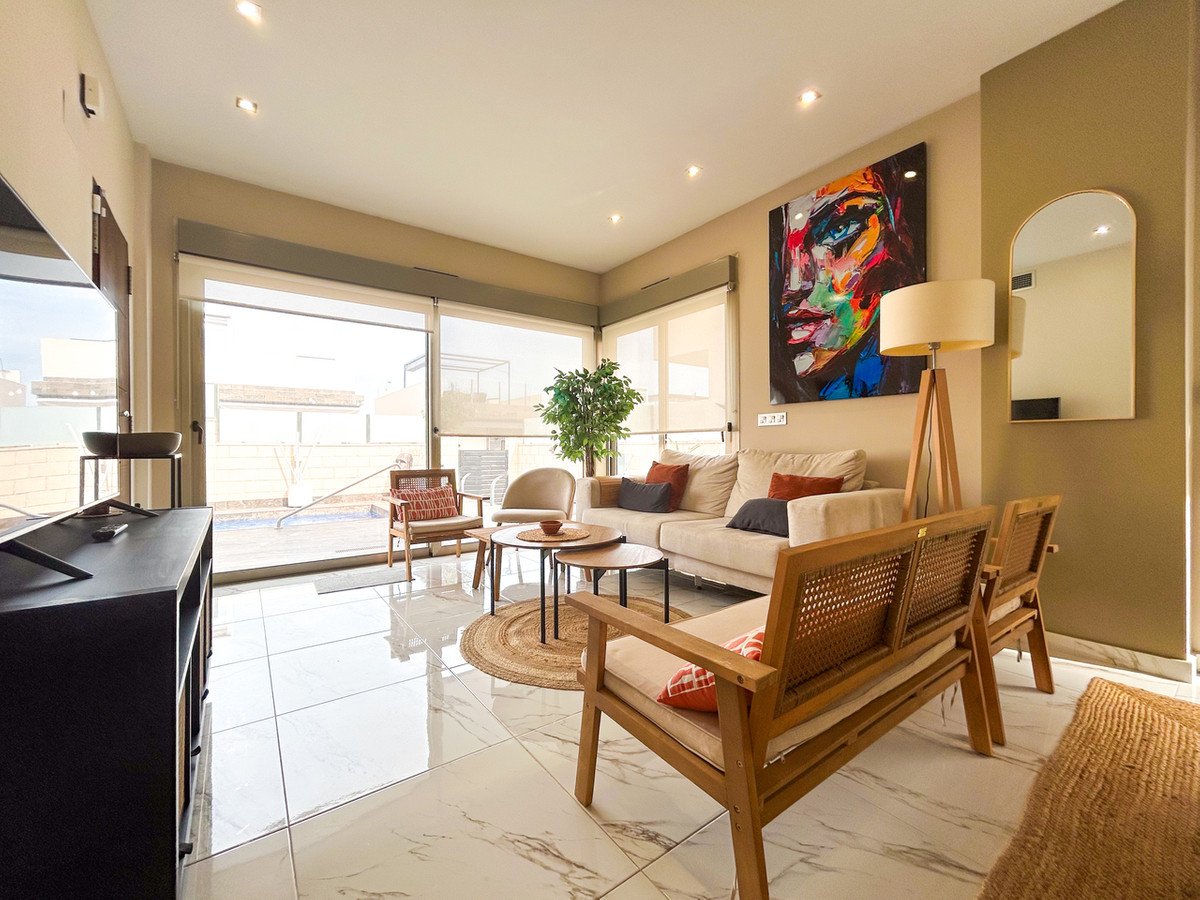 Modern living room with a sofa, chairs, large painting, and a view of a swimming pool through glass doors.