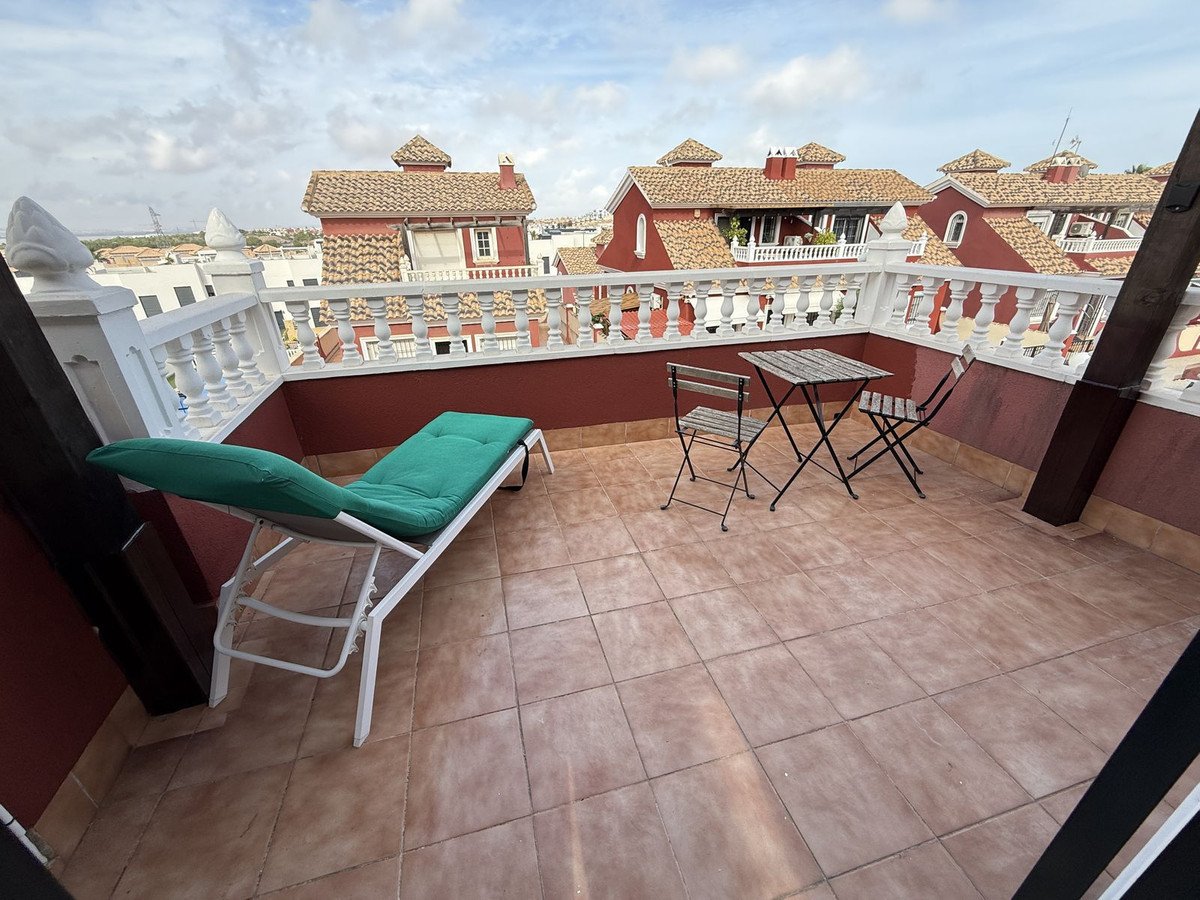 Spacious terrace with a lounge chair and small table, overlooking terracotta-roofed buildings under a cloudy sky.