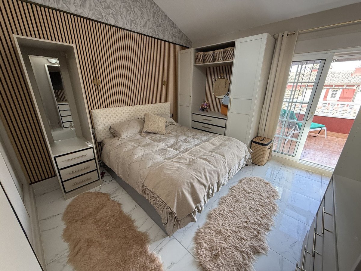 Modern bedroom with wooden accent wall, king-size bed, fluffy rugs, and access to a sunny terrace.