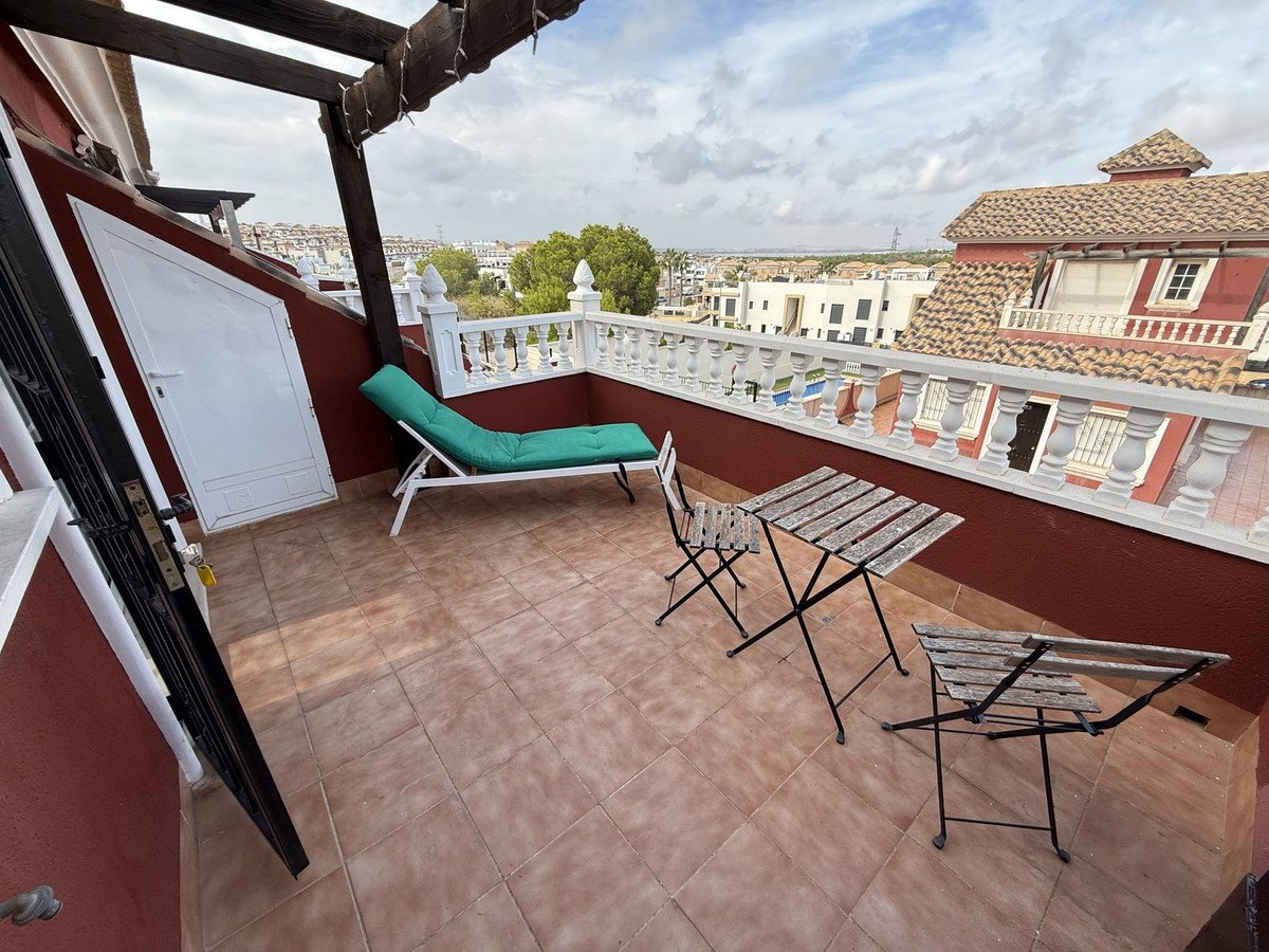 Terrace with a lounge chair and a small table and chairs, overlooking rooftops and a distant landscape.