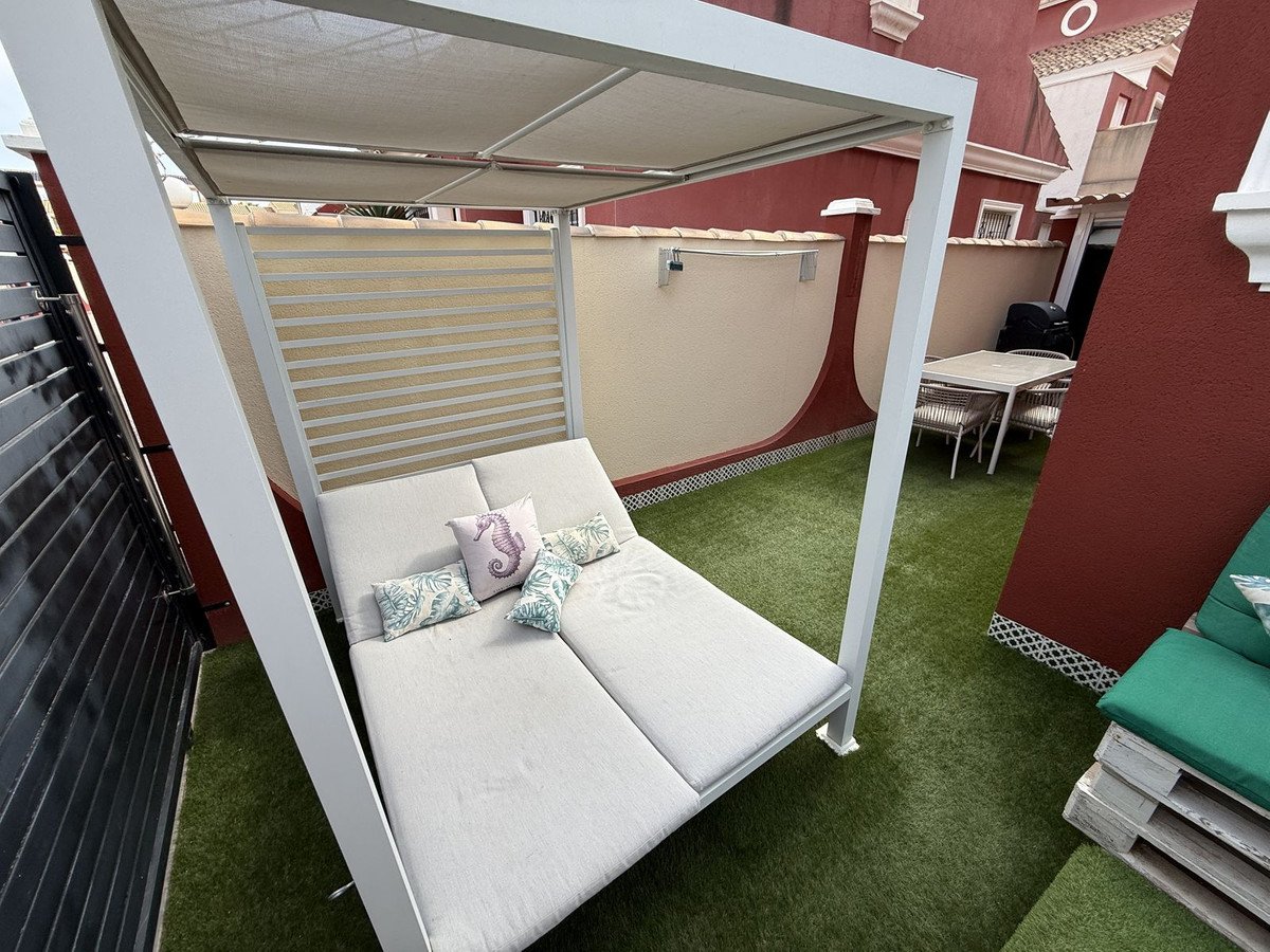 Outdoor terrace with a double daybed, dining table with chairs, and a barbecue. Artificial grass flooring.