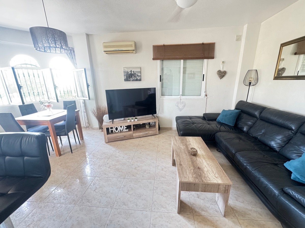 Spacious living and dining area with a black leather sectional sofa, TV, and dining table by large windows.