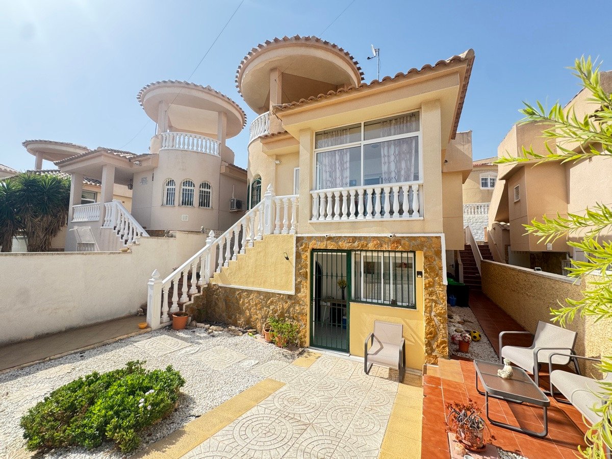 Exterior of a multi-story villa featuring a prominent staircase, a private patio with seating, and a sunny sky.