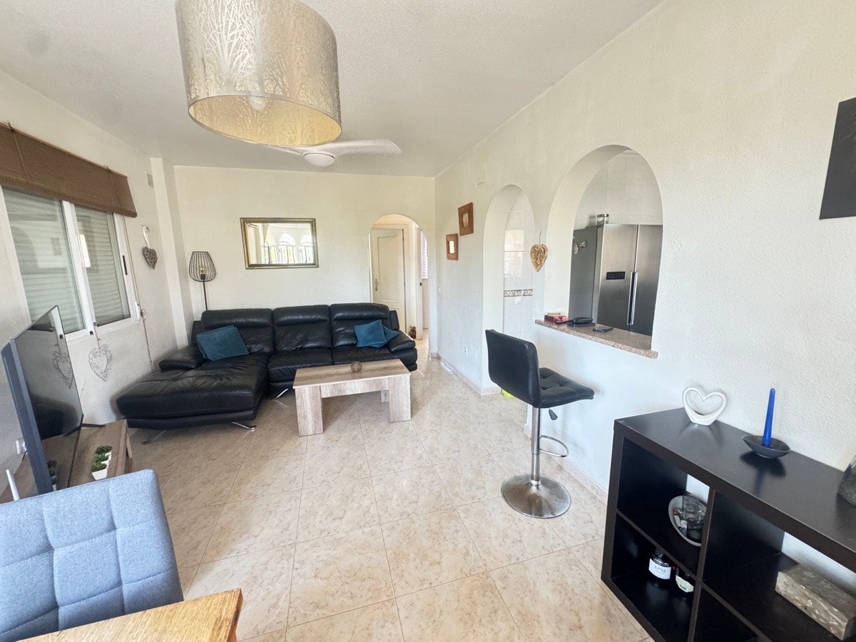Modern living room with a black leather sectional sofa, coffee table, and an open-plan kitchen with a breakfast bar.