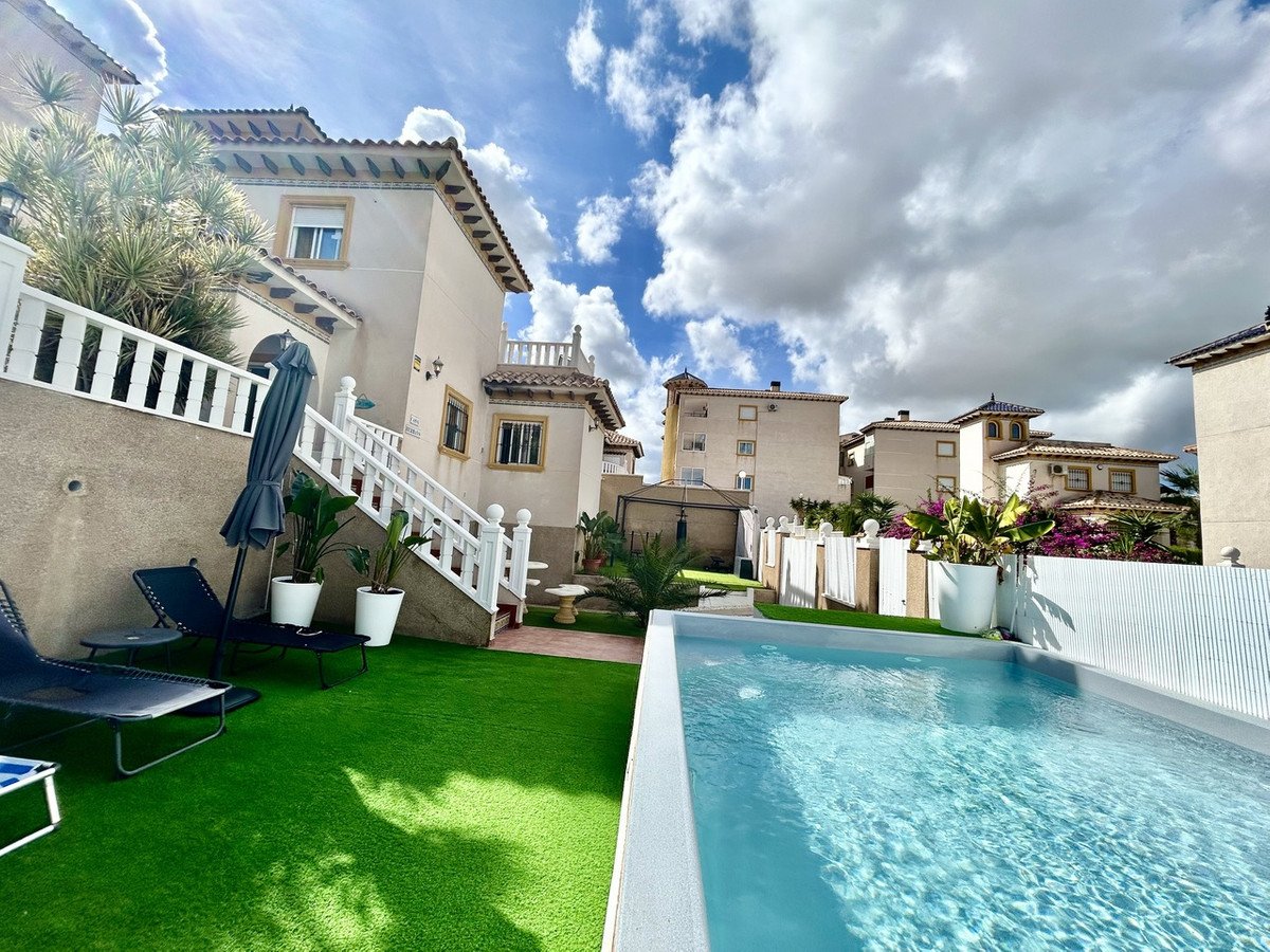 Backyard of a villa with a swimming pool, lounge chairs, and green lawn.