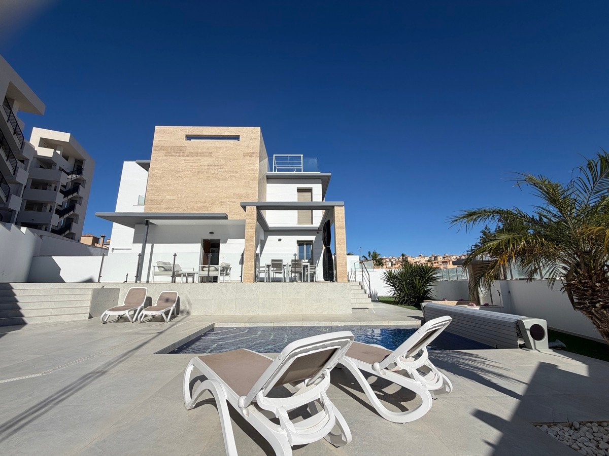 Modern villa with a private pool, sun loungers, and a terrace, surrounded by palm trees and clear blue sky.
