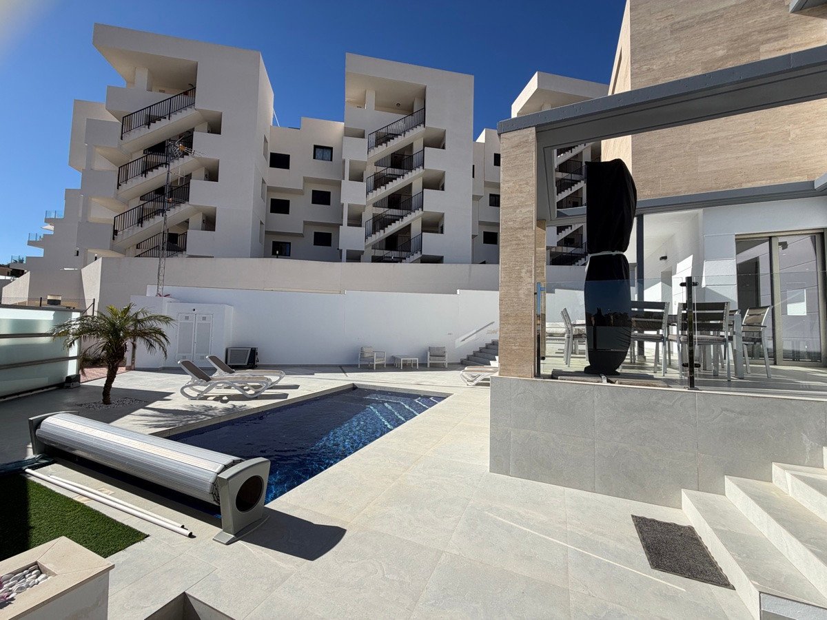 Modern villa terrace with a private pool, lounge chairs, and outdoor dining area. Modern apartment buildings in the background.