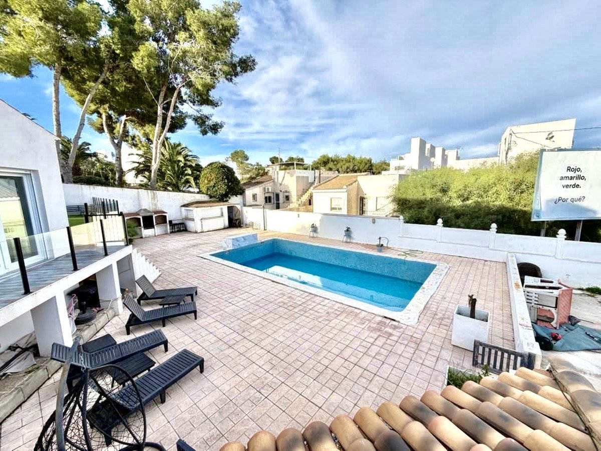 Outdoor pool area with sun loungers, trees, and a sign with Spanish text in the background.