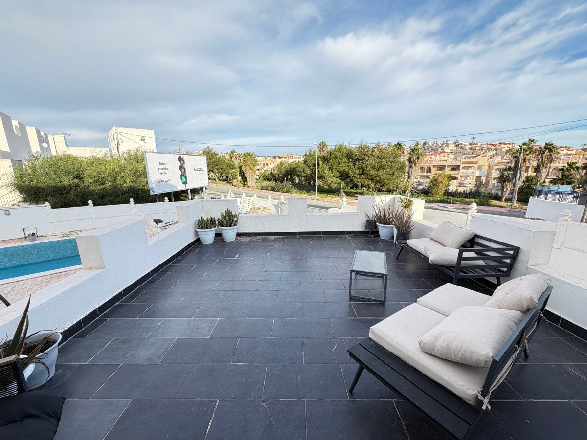 Modern terrace with lounge chairs, a small pool, and a view of houses and palm trees.