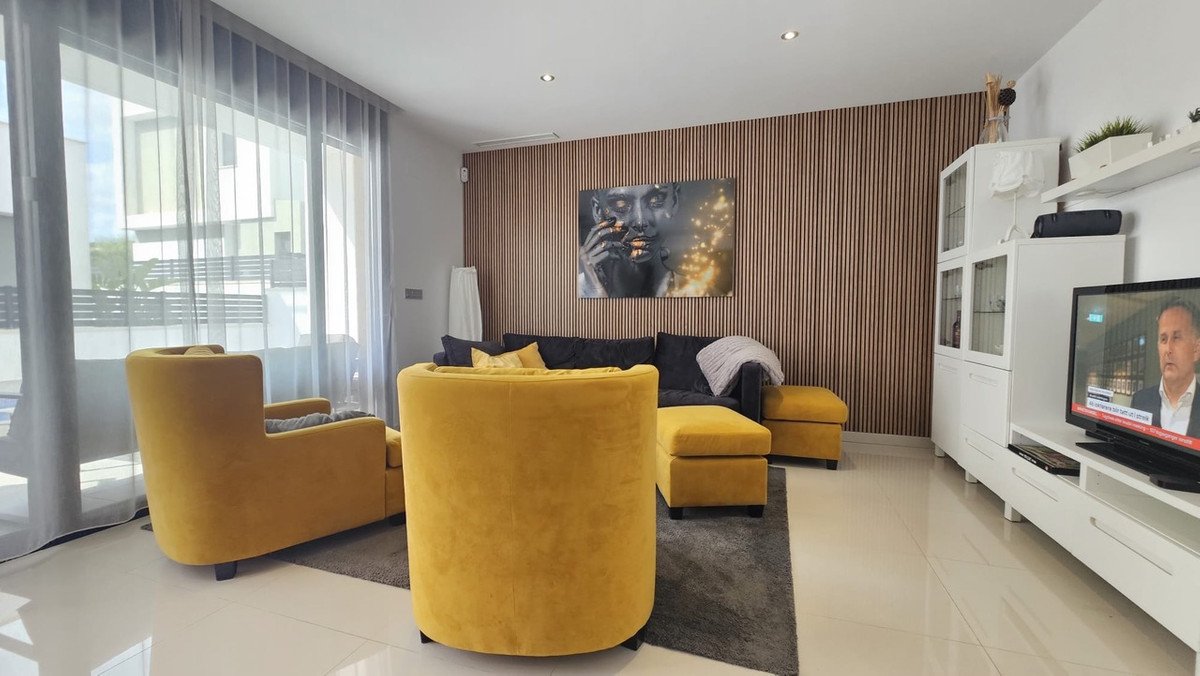 Modern living room with yellow chairs, dark grey sofa, wooden accent wall, and large windows with sheer curtains.