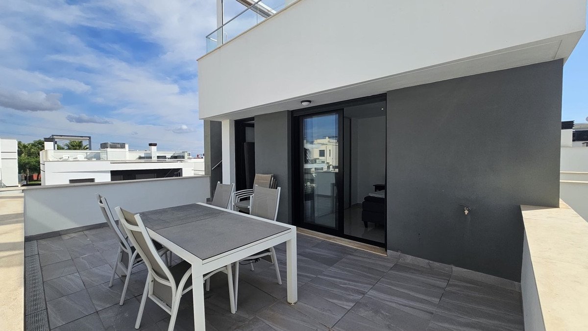 Modern terrace with a dining table and chairs, overlooking a contemporary building complex and a cloudy sky.
