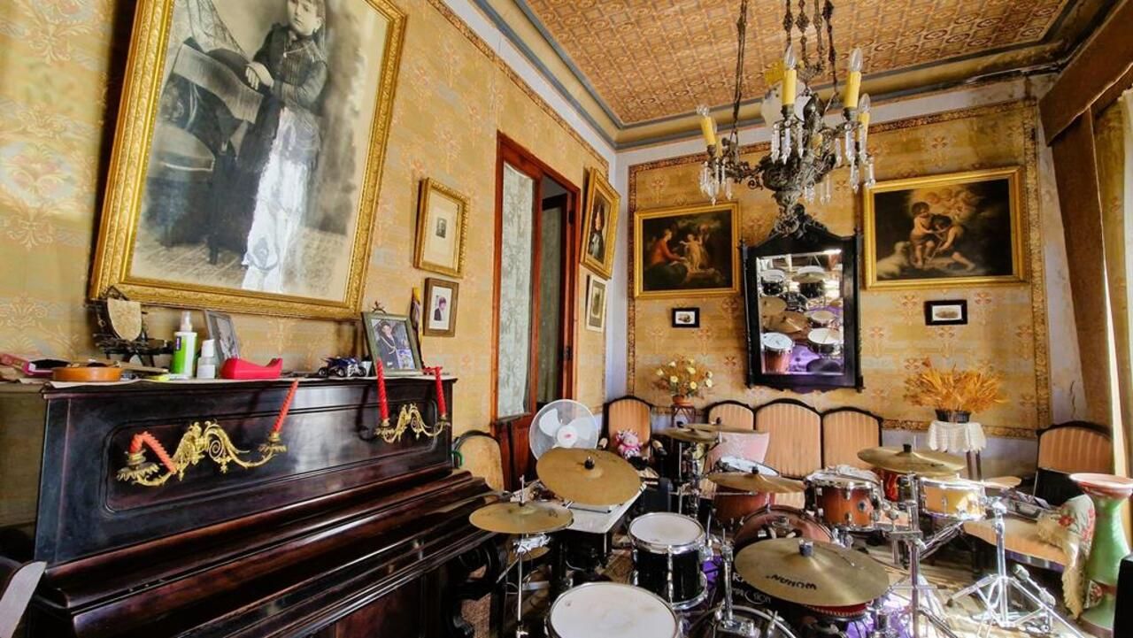 Eclectische kamer met piano, drumstel en vintage decoratie.