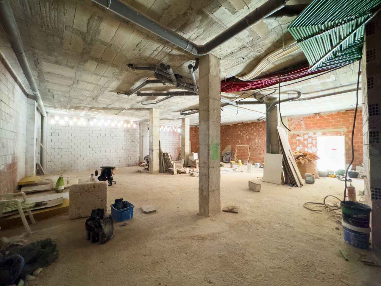 Onvoltooide interieur bouwplaats met betonnen pilaren en zichtbare leidingen.