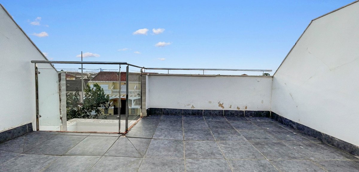 Spacious tiled terrace with glass balcony railing and a view of neighboring houses under a blue sky.