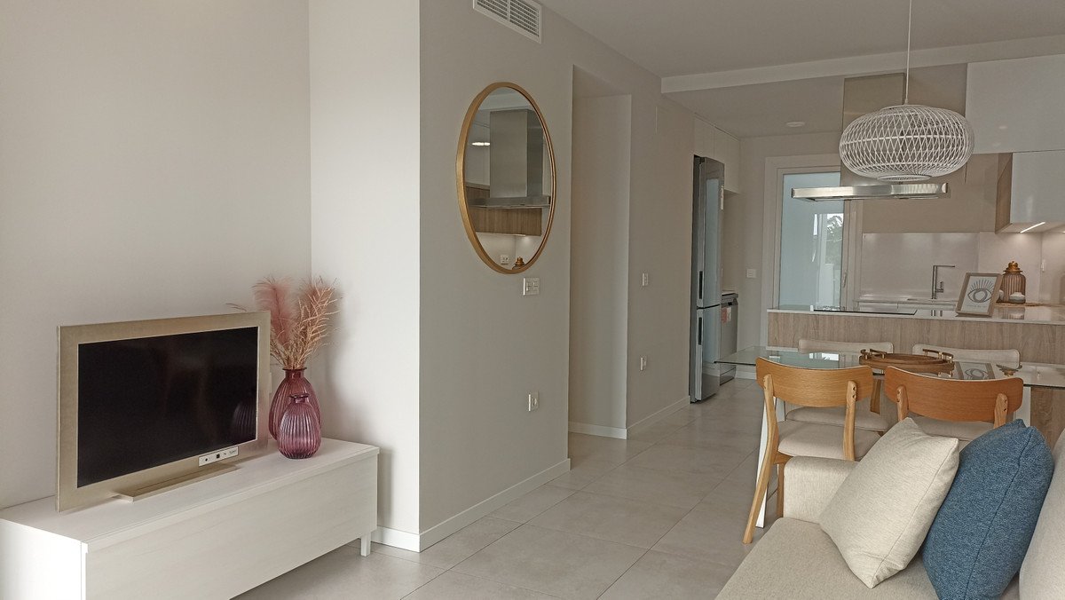 Modern open-plan living, dining, and kitchen area with a sofa, dining table, and kitchen island. Features a TV and decorative elements.
