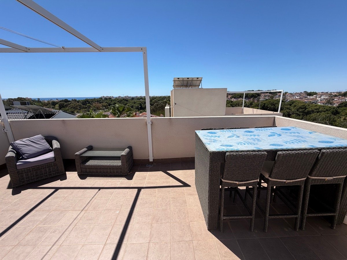 Outdoor terrace with dining table, chairs, and lounge seating with a distant sea view under a clear blue sky.