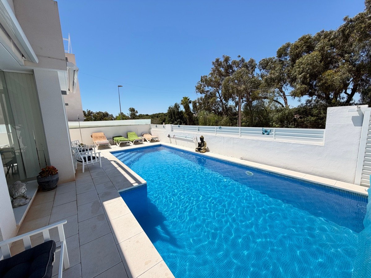 A private swimming pool with loungers and trees in the background under a clear blue sky.