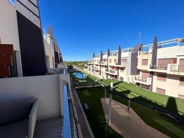 Modern apartment buildings with balconies overlooking a communal pool and green lawn area under a clear blue sky.