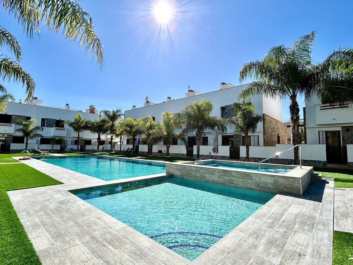 Resort pool area with sunny sky, palm trees, and modern buildings.