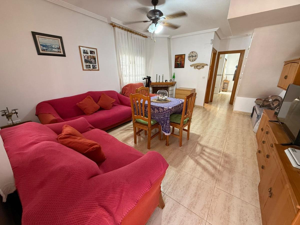 A cozy living and dining area with red sofas, a dining table, and wooden furniture, leading to a hallway.