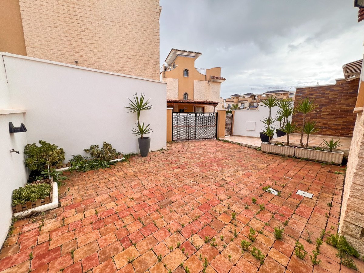 A paved terrace area with planters, plants, and a gate leading to houses.