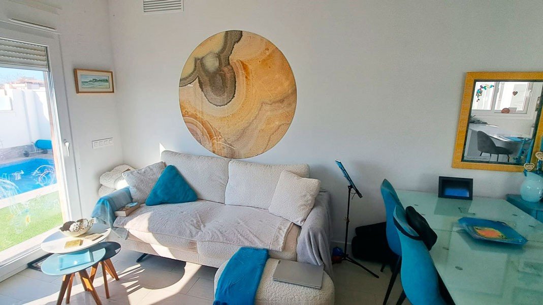 Bright living room with a sofa, artwork, and a view of the swimming pool through the glass door.