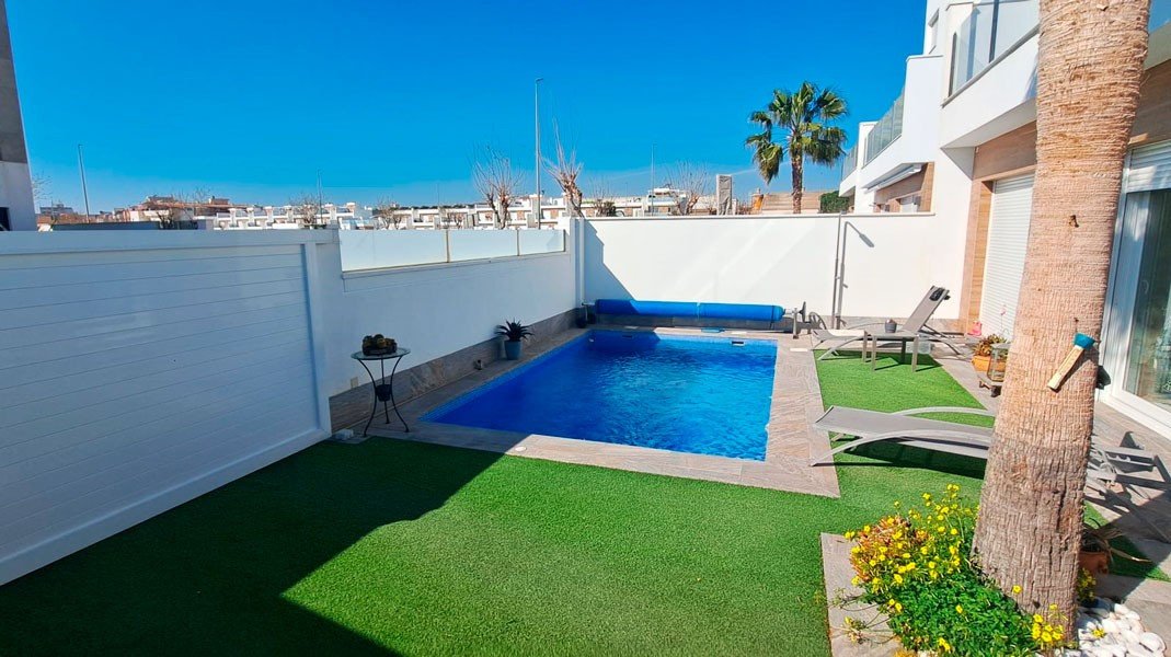 Modern villa with a private swimming pool, sun loungers, artificial grass, and outdoor shower on a sunny day.