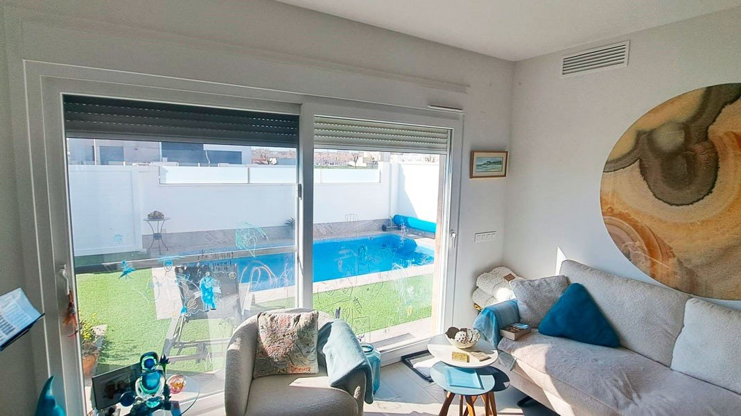 Interior living room with sofa and armchair, overlooking a private swimming pool and garden through large sliding glass doors.