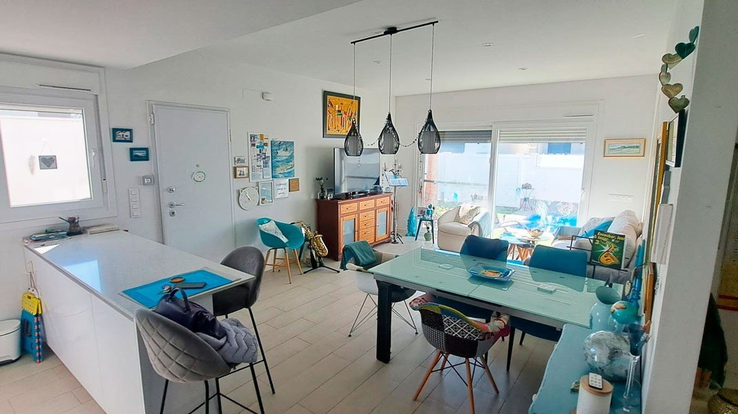 Modern open-plan living, dining, and kitchen area with a white island, glass dining table, and lounge area with a large window.