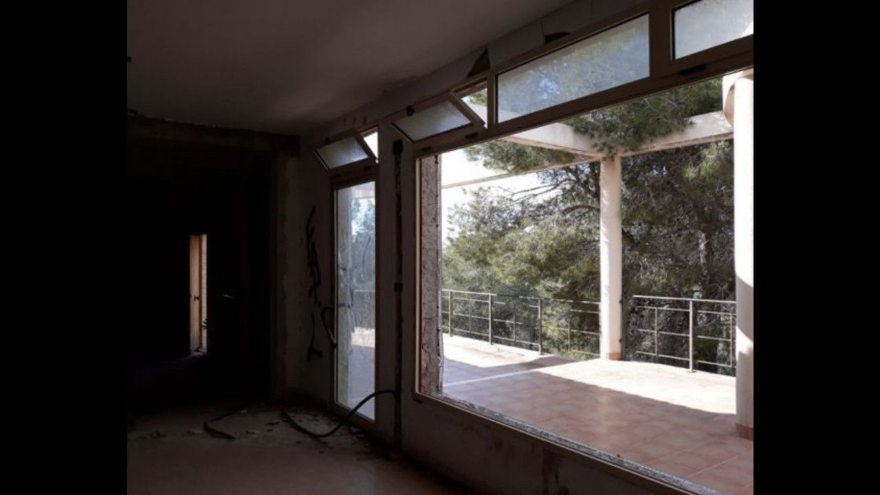 Interieur van een verlaten huis met uitzicht op een terras en bomen.