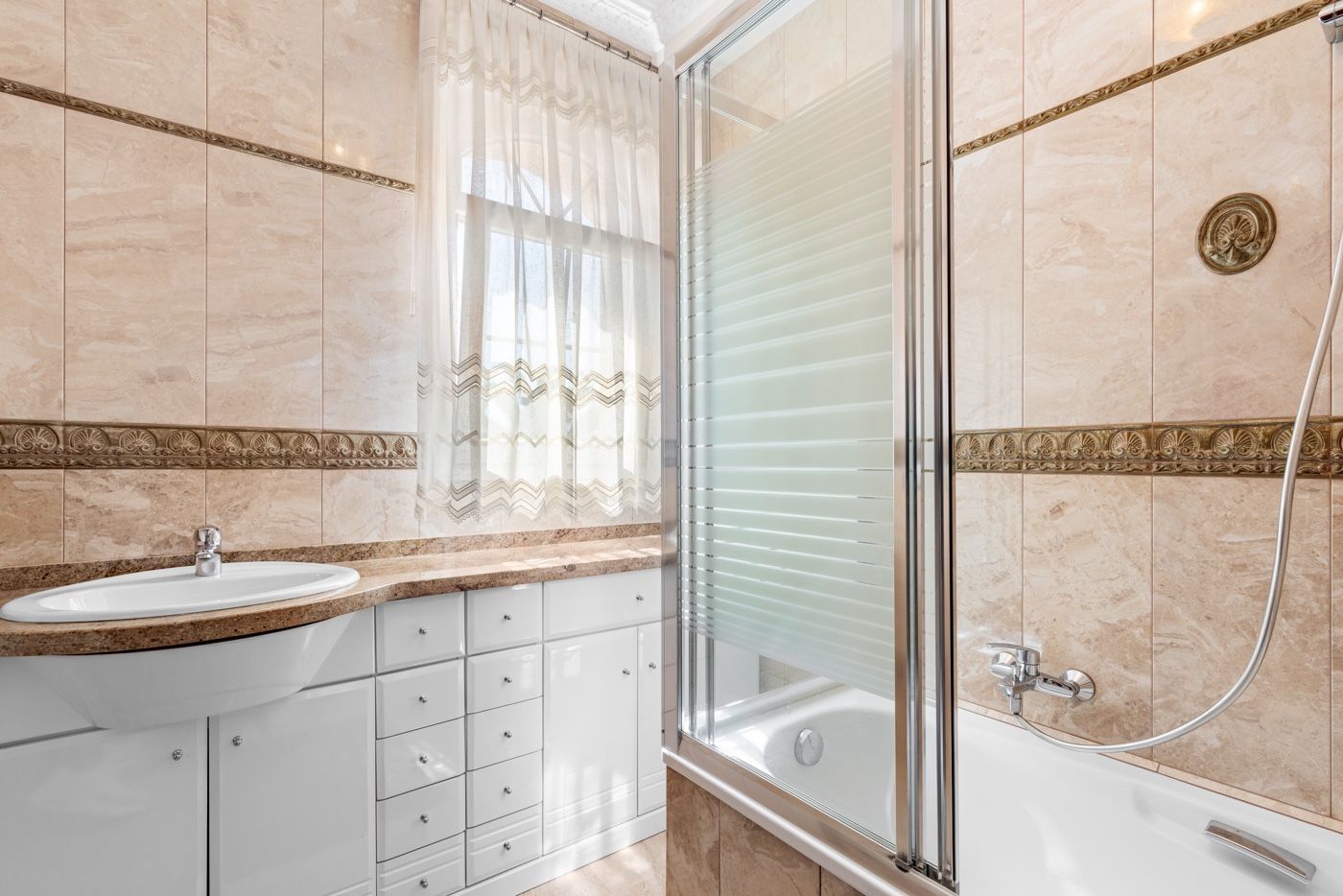 Badkamer met beige tegels, bad en wastafel