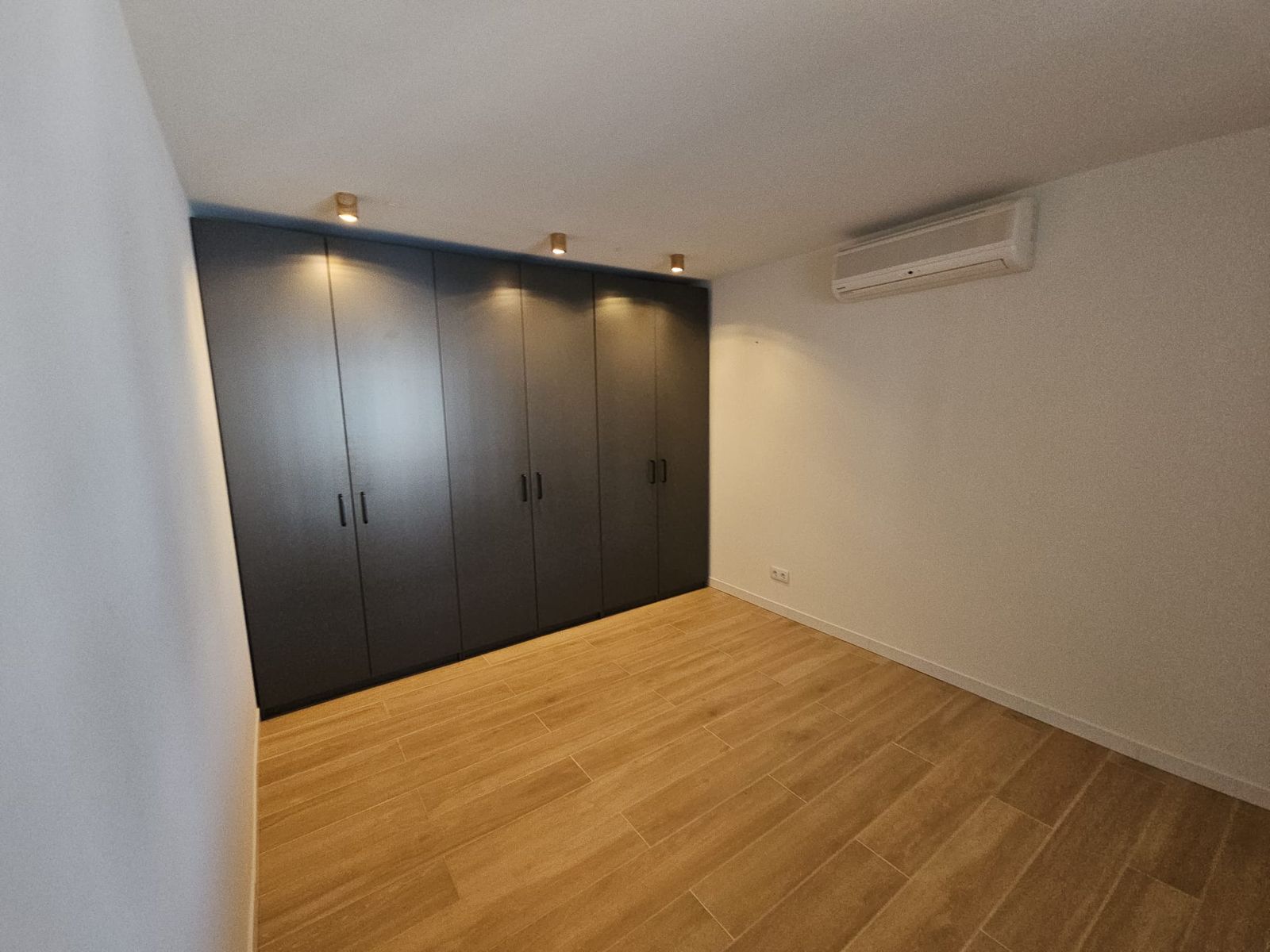 Moderne slaapkamer met grote, donkere kledingkast en houten vloer.