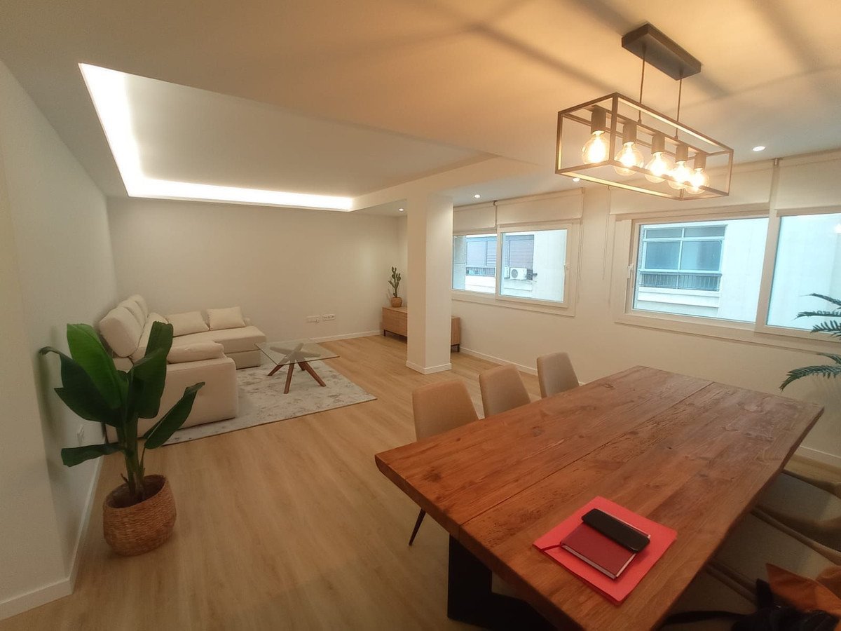 Modern living and dining area with a sectional sofa, large wooden table, and large windows offering natural light.