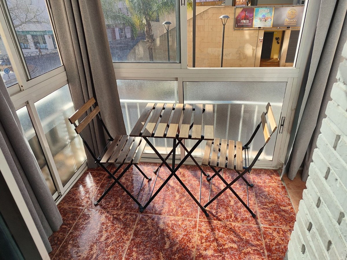 A small outdoor dining set with a wooden table and two chairs on a balcony overlooking a street and buildings.