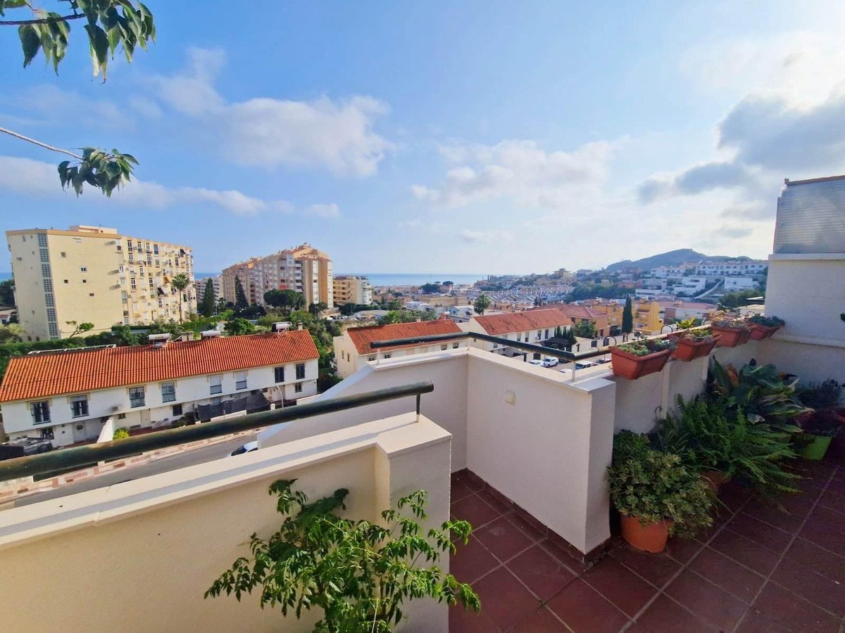 Balcony with red tile floor, potted plants, and a panoramic view of a coastal city and sea under a blue sky.