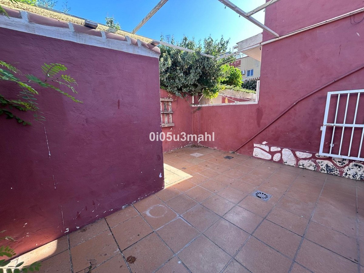 Tiled courtyard with a maroon wall, some greenery, and a white barred window. Outdoor space with a drain on the floor.