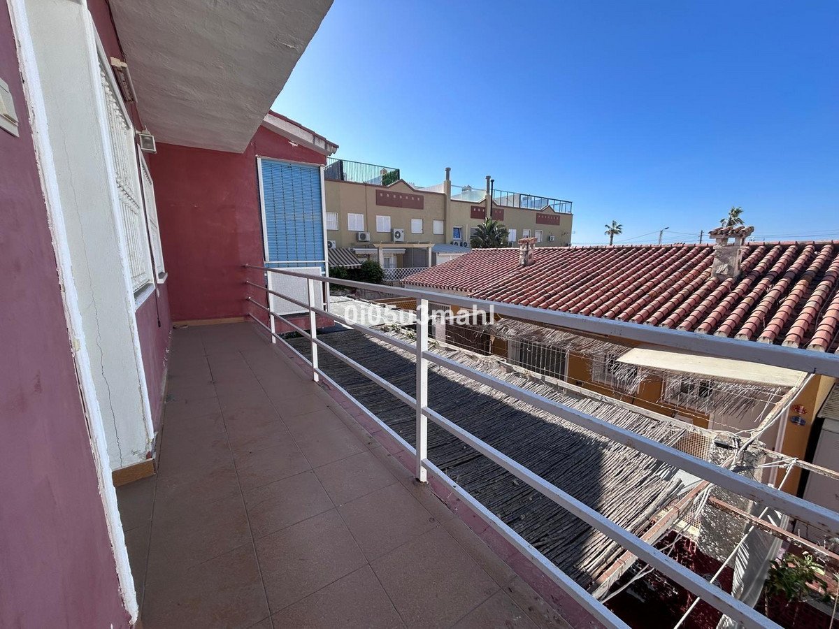 A tiled balcony overlooks rooftops under a clear blue sky, with neighboring houses visible.
