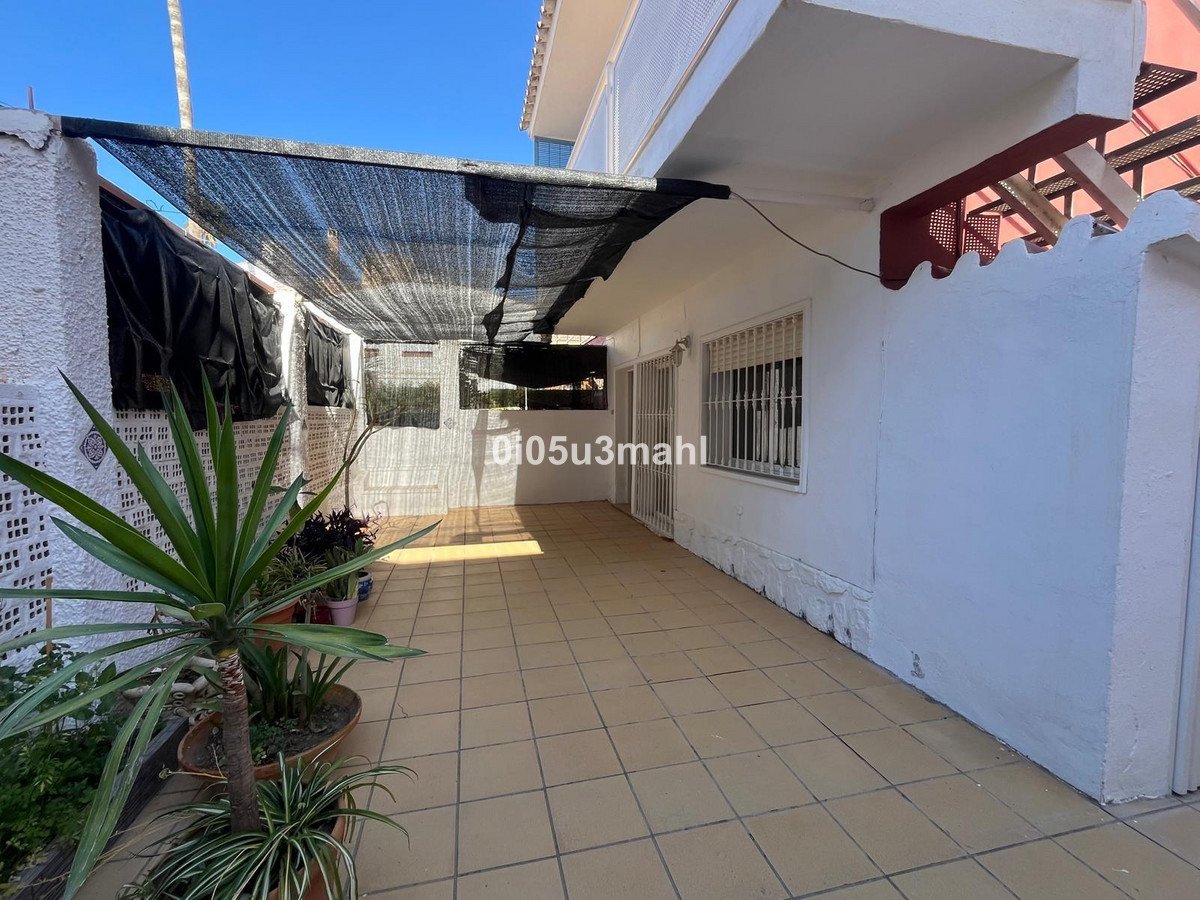 Tiled patio with a black shade cover, plants, and white walls. Outdoor living space.
