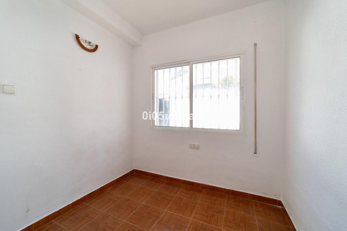 A simple room with tiled flooring and a window with security bars looking out to a bright exterior.