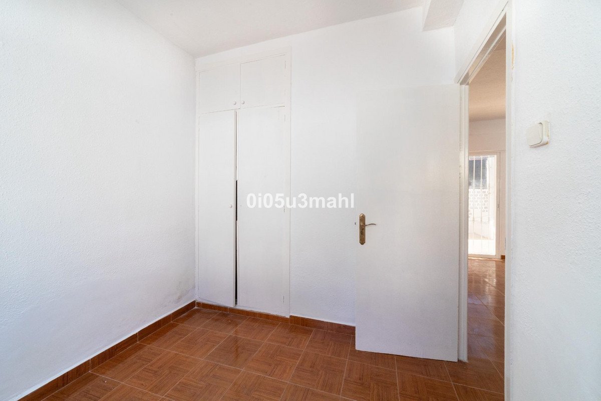 A simple bedroom featuring white walls, built-in closets, and tiled flooring, with a doorway leading to another room.